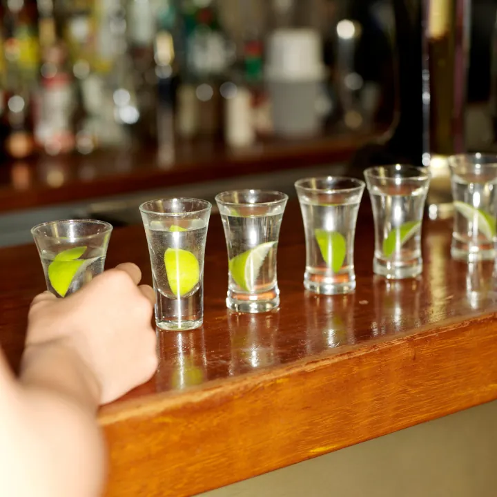A row of shot glasses with a lime in each laid out across a bar.