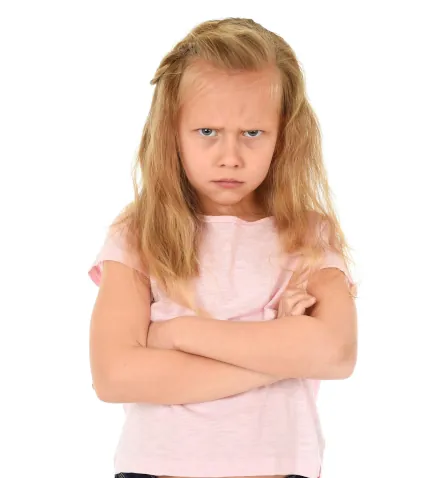 A young girl expresses her displeasure, arms crossed and brows furrowed, in a mix of frustration and determination. Her reddish blonde hair frames her serious expression, hinting at a story behind her mood.
