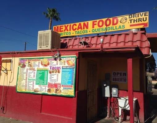 Very small Mexican food restaurant with large menu board, and drive thru sign.  A sink and electrical wiring are at the entrance.