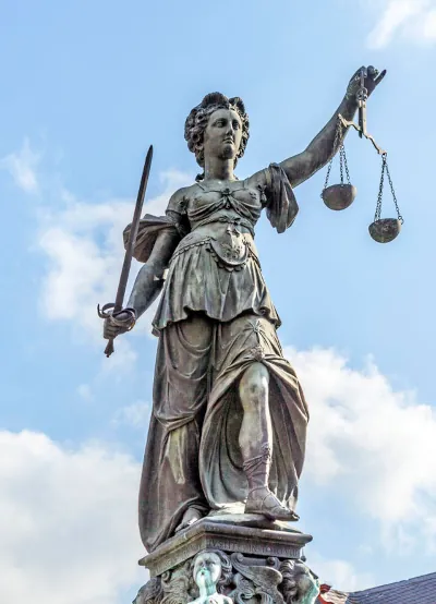 Statue of Justice at Old Bailey Courthouse with raised scales and sword.  Justice isn't blindfolded