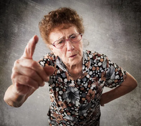 An elderly woman with a stern expression gestures emphatically, likely expressing her disapproval with a sense of authority. Her floral-patterned shirt adds a touch of vibrancy to the serious tone of the moment, highlighting both wisdom and determination.
