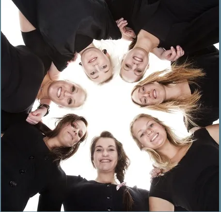 Several women standing in a circle looking inward and downward portraying teamwork and unity